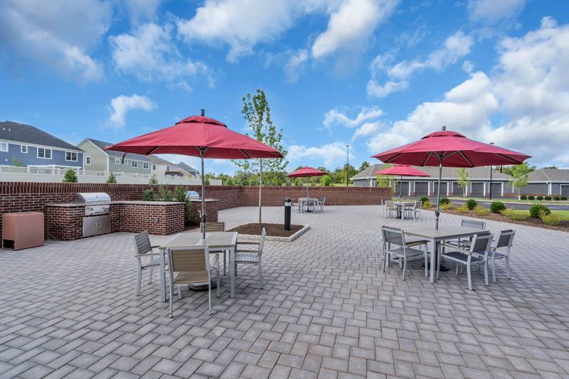 Exterior photo of Meadows at Montgomery showing the large outdoor paver patio with multiple tables and chairs and grilling stations.