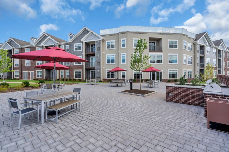 Exterior photo of Meadows at Montgomery showing the large outdoor paver patio with multiple tables and chairs and grilling stations.