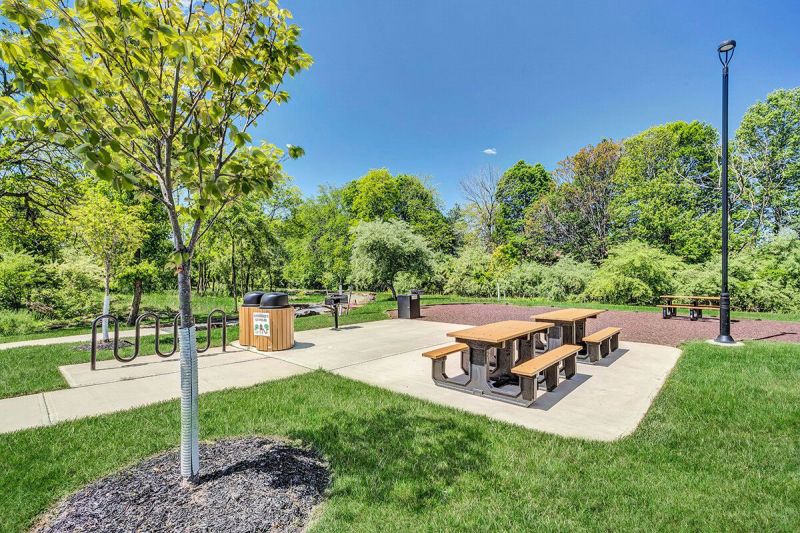 River Links exterior photo showing one of the properties outdoor grilling areas. There are several grills and picnic tables on a stone patio for residents use. There is also a bike rack and several garbage cans.