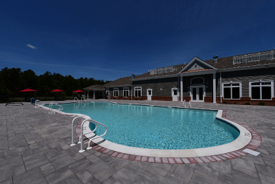 Gardens at Jackson Twenty Swimming Pool photo with a fence around the pool and patio area. The Club House can be seen in the background. Several bushes and trees highlight the landscape.