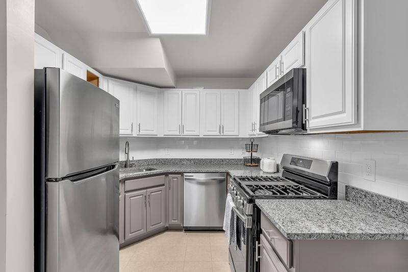 Interior photo of the kitchen at Meridian Terrace showing modern grey and white cabinetry, grey granite tops, stainless steel appliances and ceramic tile flooring.