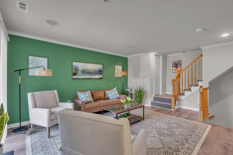 Interior photo of the living room at Meridian Terrace showing modern white oak flooring, a couch and two chairs with a coffee table. A carpeted staircase with railings can be seen leading to the upper and lower level of the unit