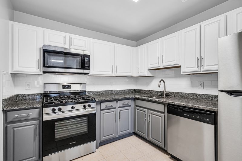 Interior photo of the kitchen at Meridian Terrace showing modern grey and white cabinetry, grey granite tops, stainless steel appliances and tile flooring.
