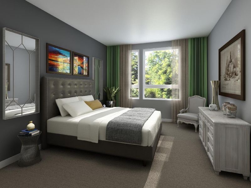 Next at Xchange interior photo of master bedroom shows king sized bed with large head board, two night tables located on either side and dresser. Single arm chair and large window with floor to ceiling drapes can be seen in the background.