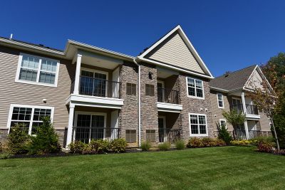 Exterior photo of the exterior of an apartment building in the affordable housing section at The Club at Woodhaven, showing a 2 story building with tan siding, white trim and windows and mixed stone. Lush landscaping surrounds the area.