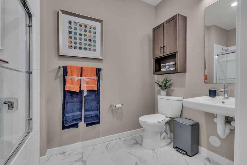 Photo of bathroom at Edison lights showing tub with glass shower doors, toilet with medicine cabinet above, sink with mirror above and designer tile flooring.