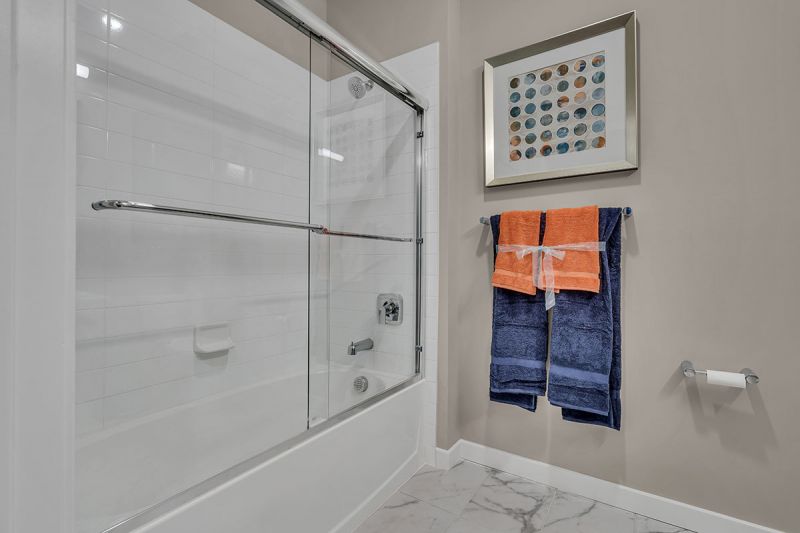 Photo of bathroom at Edison lights showing tub with glass shower doors and designer tile flooring.