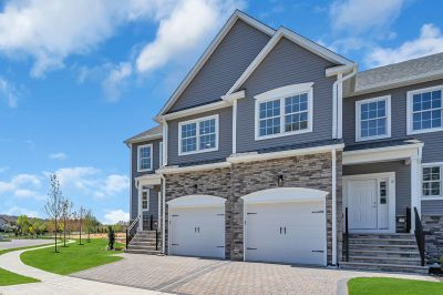 Exterior image of a townhome at the Club at Woodhaven showing gray siding with white windows, mixed brick and a 1 car garage. There is a paver stone driveway, new sidewalks and landscaping.
