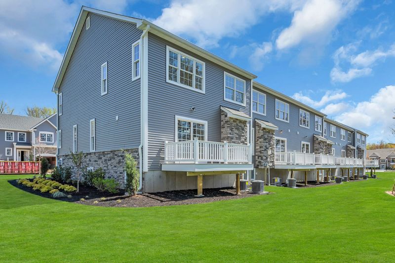Exterior image of the back of a townhome at the Club at Woodhaven showing gray siding with white windows and a large private deck for each unit