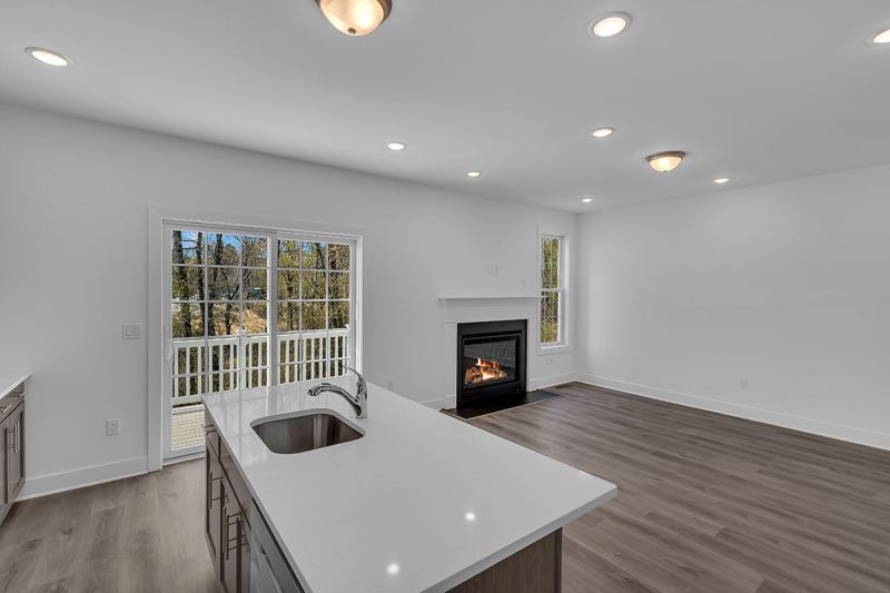 Interior image of a townhome at the Club at Woodhaven showing the view from the kitchen into the living room in which you see the kitchen island, the luxury vinyl plank flooring, fireplace and sliding glass doors leading to the deck.