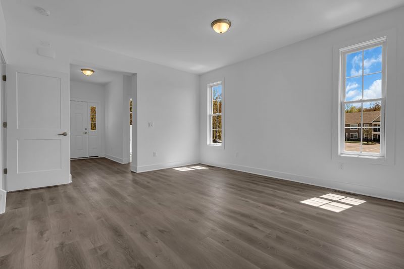 Interior image of a townhome at the Club at Woodhaven showing the interior with 2 large windows, luxury vinyl plank flooring and the entry door.