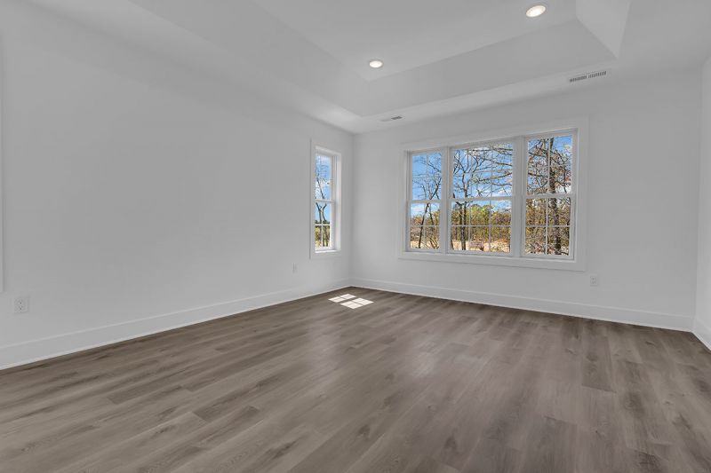 Interior image of a townhome at the Club at Woodhaven showing the primary bedroom with luxury vinyl plank flooring and 2 large windows to allow for natural light.