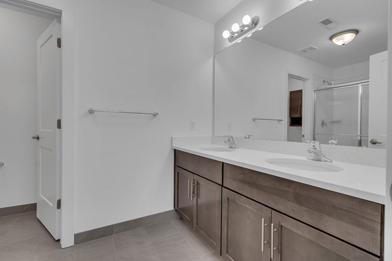 Interior image of a townhome at the Club at Woodhaven showing the primary bathroom with luxury tile flooring, vanity with dual sings and large mirror with lights.