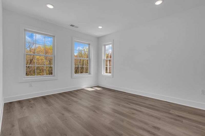 Interior image of a townhome at the Club at Woodhaven showing another bedroom with luxury vinyl plank flooring and 3 windows to allow for plenty of natural light