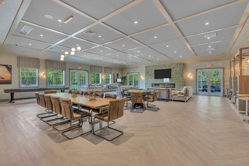 Interior photo of the community room inside the clubhouse at Woodhaven, featuring laminate wood flooring, several seating areas for congregating, a large fireplace with TV above, and several games such as foosball and a poker table.
