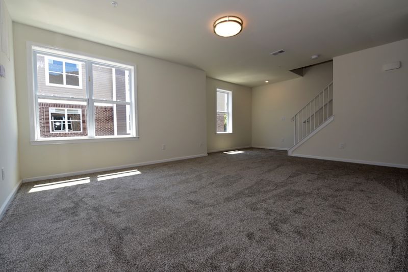 Interior photo of a family room at Harbortown Bay showing plush wall to wall carpeting, two windows to allow for natural light and stairs leading to the second floor.