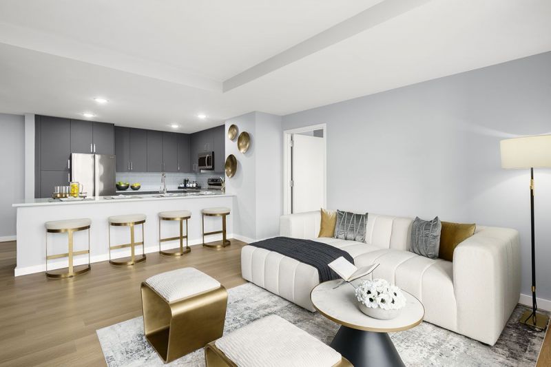 Interior photo showing a typical living room in an apartment at RVR with luxury vinyl plank flooring, a couch and 2 chairs with a coffee table. The gourmet kitchen can be seen due to the open floorplan.