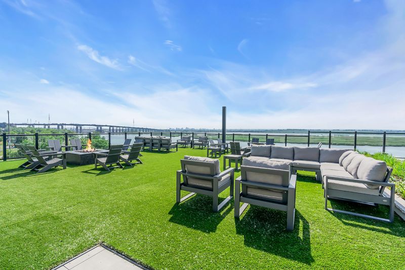 Exterior photo of the rooftop located on the 5th floor at RVR showing an additional seating area on grass including modern sectional couches and chairs. To the left is patio seating in front of a large gas fireplace.