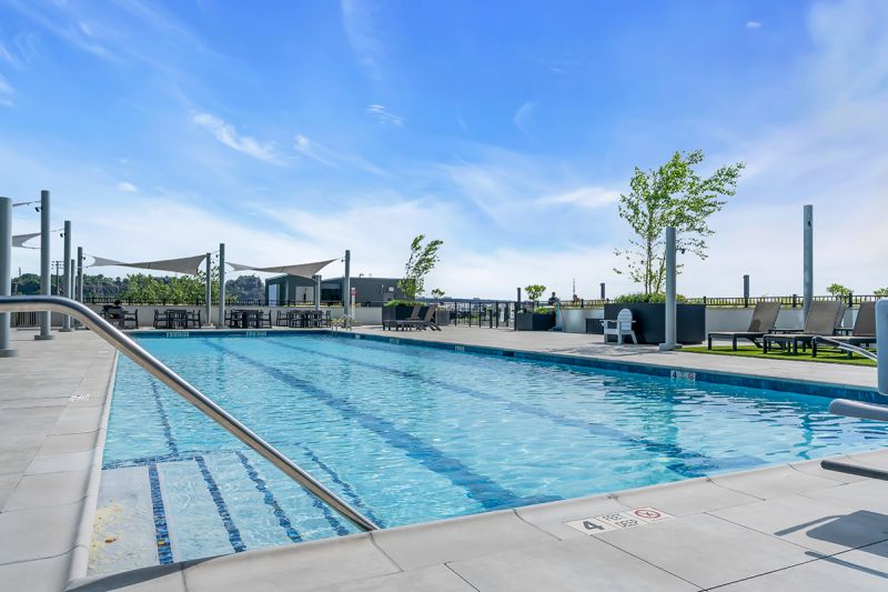 Exterior photo of the community’s pool located on the 5th floor at RVR showing another angle of a large pool with several shaded seating areas and amazing views.