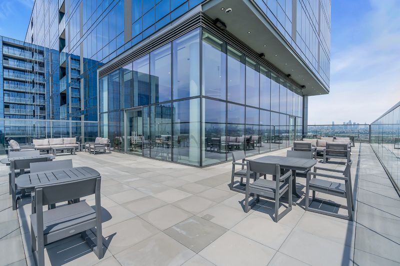 Exterior photo of the rooftop located on the 19th floor at RVR showing multiple seating areas with clear glass fences wrapped around the community building. The community building can be seen in the background.