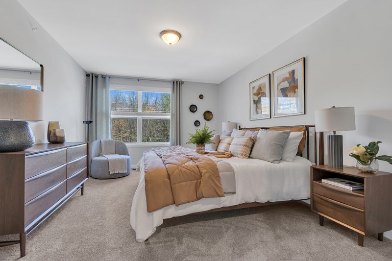 Interior photo of the Boulders at Beekman showing a primary bedroom with a bed, two night stands, dresser, chair, wall to wall carpeting and a double window to allow for natural light.