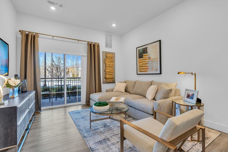Interior photo of an apartment at the Enclave at Woodhaven showing the living room with luxury vinyl wood grain flooring, couch and chair, coffee and end table with a wall mounted TV. 