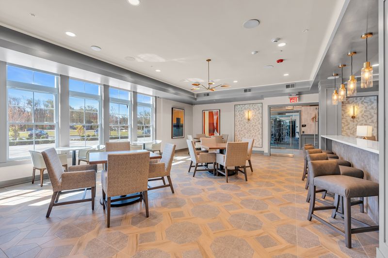 Interior photo of the resident lounge at the Enclave at Woodhaven showing several tables and seating areas of for residents to congregate.