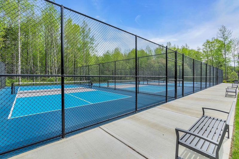 Exterior photo of the park at Enclave at Woodhaven featuring several fenced tennis courts. A concrete walking path surrounds the courts, with multiple benches placed along the route for seating.