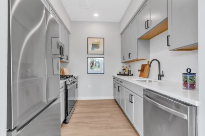 Interior photo of the kitchen at Woodland Square showing LVT flooring, grey cabinets, white Quartz countertops, and modern stainless-steel appliances.