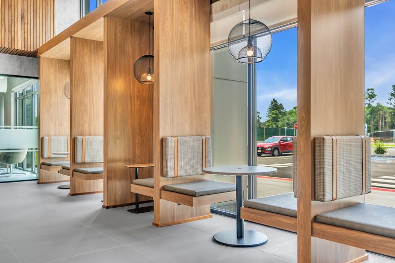 Interior photo of the community lounge at Woodland Square showing two-person seating cubicles including overhead light fixtures and large floor-to-ceiling windows. The leasing office can be seen in the background.