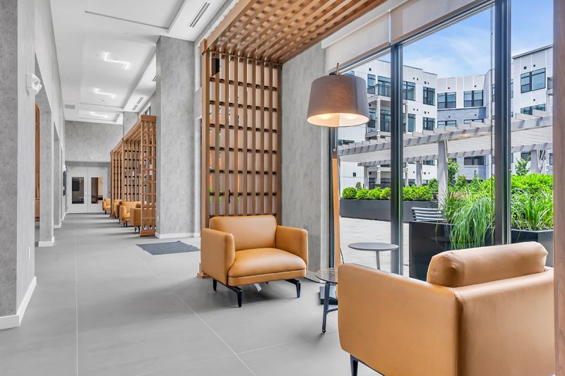 Interior photo of the lounge at Woodland Square showing two large chairs, and a small café table with a lighting fixture overlooking the exterior amenity area.