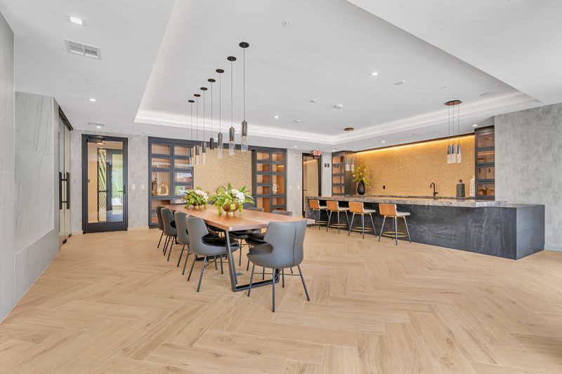 Interior photo of community room showing a professional demonstration kitchen with a large marble counter and bar-height seating. To the left of the demonstration kitchen is a large dining area seating 10 people.