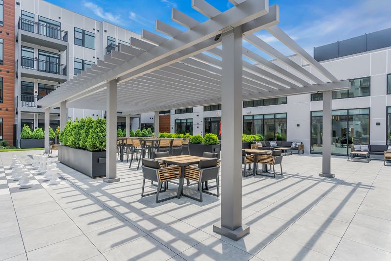 Exterior photo of the community grill at Woodland Square featuring a shaded seating area with chairs and tables overlooking the community building.