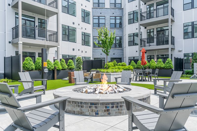 Exterior photo of the community grill at Woodland Square featuring patio seating in front of a large fireplace and additional seatings with a shaded umbrella attachment.
