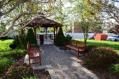 Liberty Terrace exterior photo shows the community gazebo, paver patio with benches, and the surrounding landscape with trees, bushes and flowers