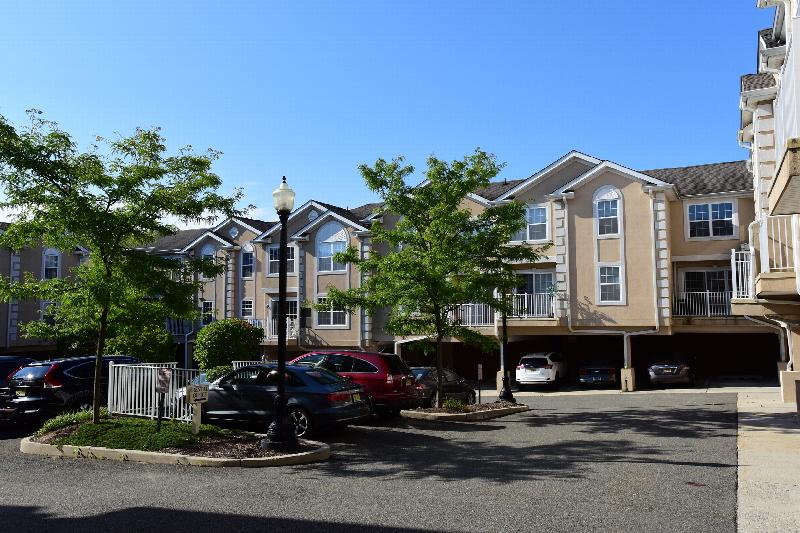 Liberty Terrace building exterior photo showing several balconies, parking lot, street light ad several trees. There is a directional sign for rental office and several no parking signs.