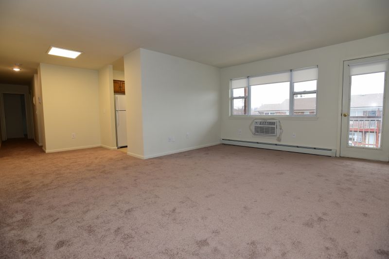 Hilltop Estates interior photo of living space showing carpeting and a large window to allow for natural light. There is a door that leads out to the balcony.