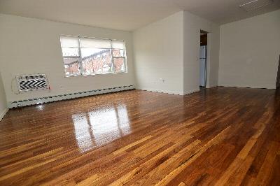 Hilltop Estates interior photo of living space showing hardwood floors and a large window to allow for natural light. There is a doorway leading into the kitchen.