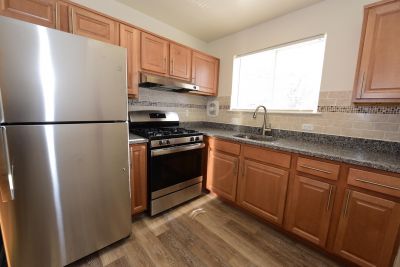 Photo of renovated kitchen showing wood grain tile flooring, new cabinets with granite counter tops and a stainless steel appliance package.