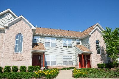 Rivendell Heights Exterior photo showing a brick and vinyl exterior. There is a pathway that leads to apartment entrances. Several bushes and trees highlight the landscape.