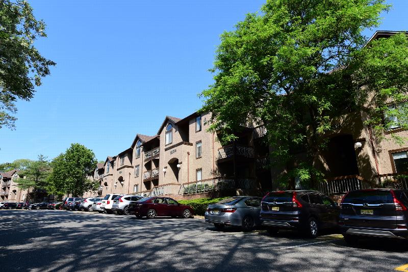 Hidden Valley exterior photo showing a large 3 story apartment building. There are balconies on each level, and several entrances are shown. Several mature trees are located on the side and in front of the building. There is a parking lot right in front of the building supplying ample parking.
