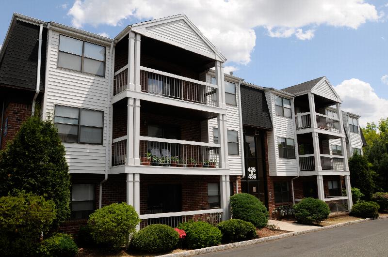 Oak Tree Village Exterior photo showing a brick and vinyl exterior and several balconies. Several trees and bushes highlight the landscape.