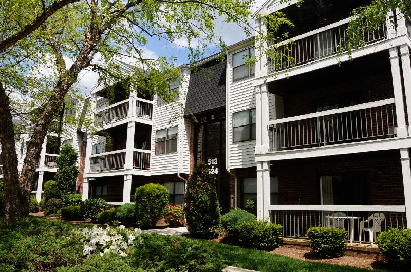 Oak Tree Village Exterior photo showing a brick and vinyl exterior and several balconies. Several trees and bushes highlight the landscape.