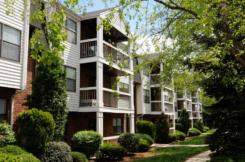 Oak Tree Village Exterior photo showing a brick and vinyl exterior and several balconies. Several trees and bushes highlight the landscape.