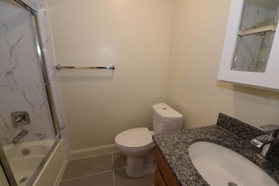 Photo showing a freshly painted renovated bathroom showing new ceramic tile flooring, new tub with shower doors, new toilet, sink, vanity and medicine cabinet.