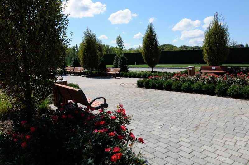 Helix at Xchange exterior photo shows tree lined community courtyard with concrete paved walkway and several park benches for seating. Courtyard is surrounded by garden style shrubs, and tree lined streets.