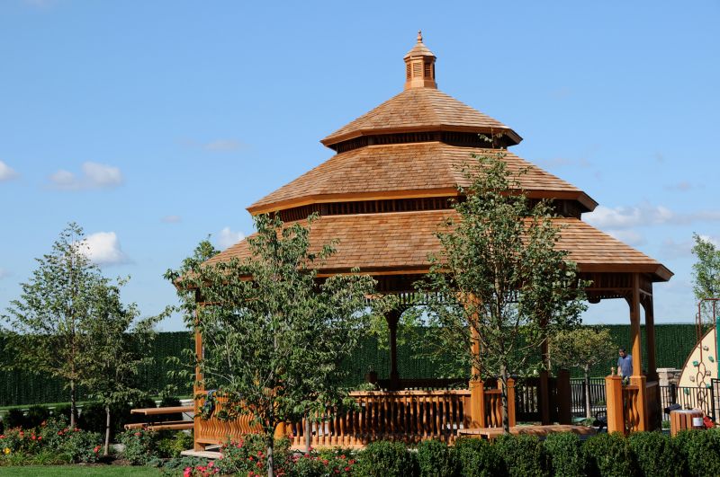 Helix at Xchange exterior photo shows large gazebo lined with garden style shrubs, trees, and park bench for seating.