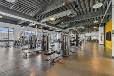 Interior photo of the gym at Xchange at Secaucus featuring a variety weights, dumbbells, barbells, and weight plates. It includes benches, squat racks, and lifting platforms to accommodate different workouts. Rubber flooring provides durability and safety, while large mirrors help users monitor their form. The space is brightly lit and neatly organized with storage racks.