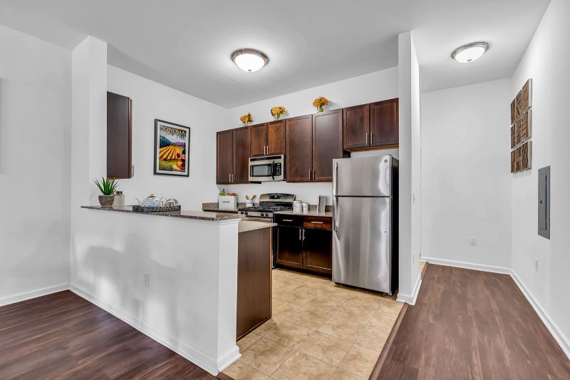 Interior photo of a model at Helix at Xchange showcasing the kitchen featuring luxury slate tiles. The kitchen includes new wood cabinetry, granite countertops, stainless steel appliances. A small hallway is visible on the right, providing access to additional areas of the unit.