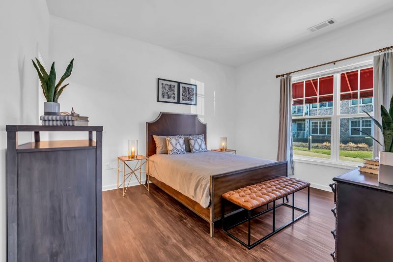 Interior photo of a model unit at Helix at Xchange highlighting a bedroom with luxury hardwood flooring and a large window that fills the space with natural light. The room is furnished with a bed, side tables and a dresser, creating a cozy and functional layout.